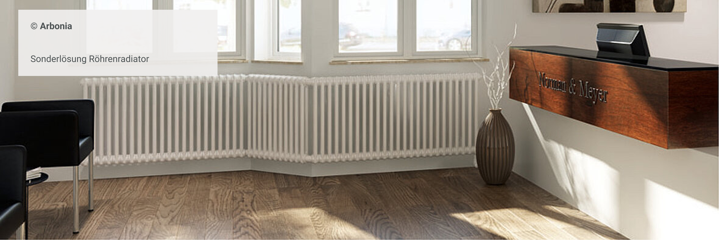 Sonderlösung Röhrenradiator: weißer Heizkörper im Eckbereich einer Fensterfront mit Holzfußboden und modernem Empfangstresen