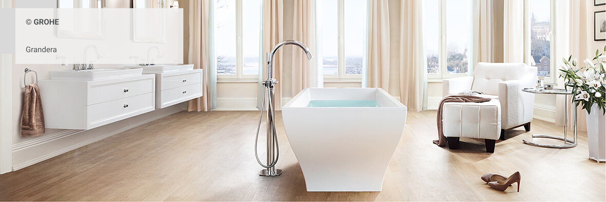 Modernes, elegantes Badezimmer mit freistehender, quadratischer Badewanne, luxuriösem Sessel und stilvoller GROHE Grandera Armatur vor großen Fenstern mit Blick ins Freie