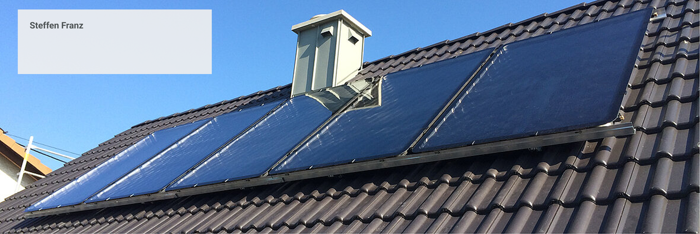 Solarthermieanlage mit Flachkollektoren auf Ziegeldach bei strahlend blauem Himmel